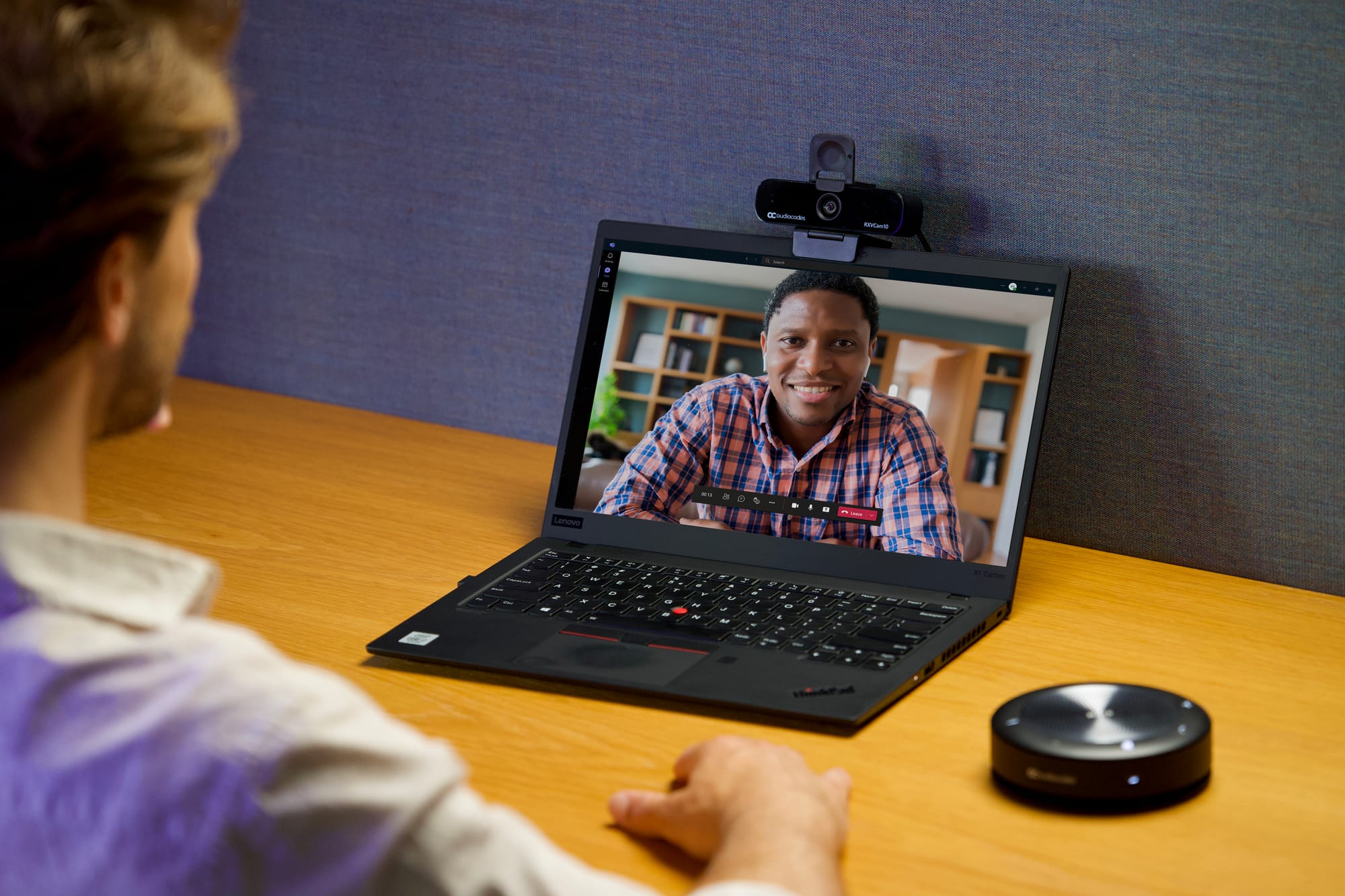 Two men speaking, one featured in person at his desk in person with the other speaking remotely via Teams